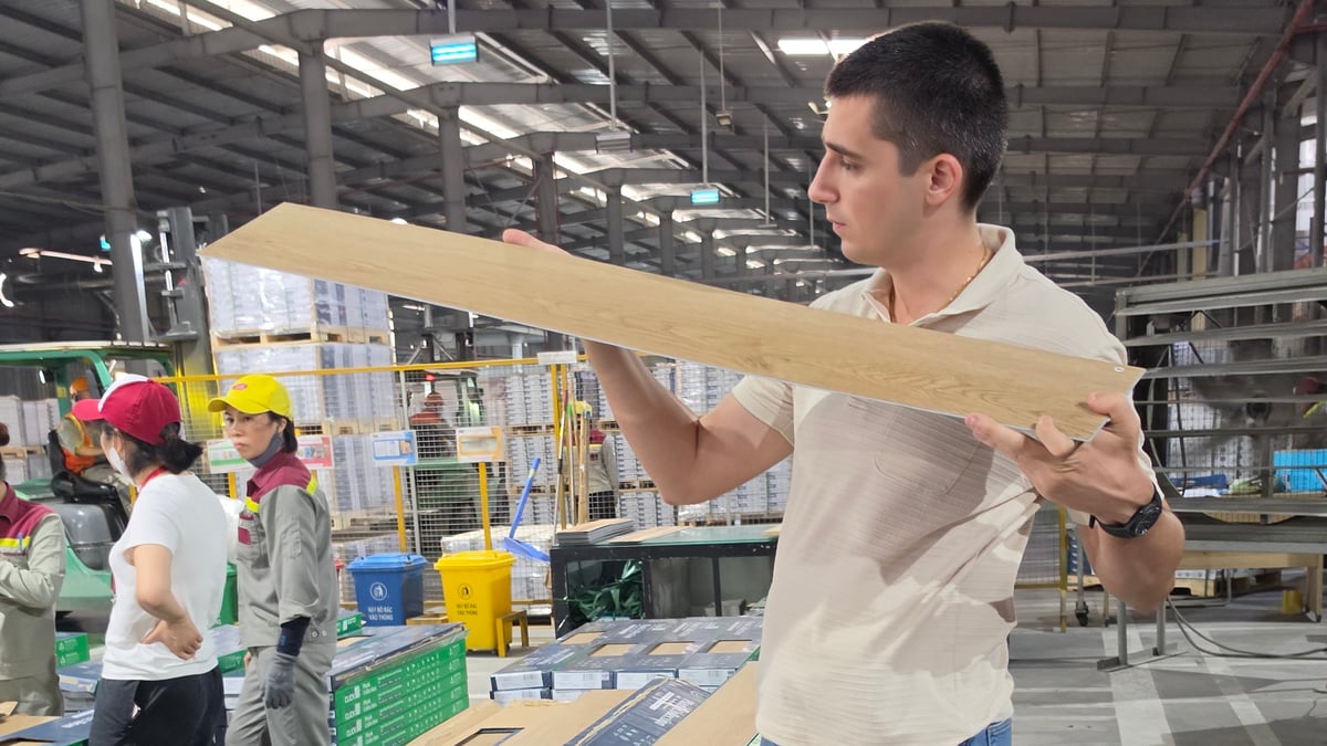 A person examining a flooring plank beside production machinery on a factory floor.